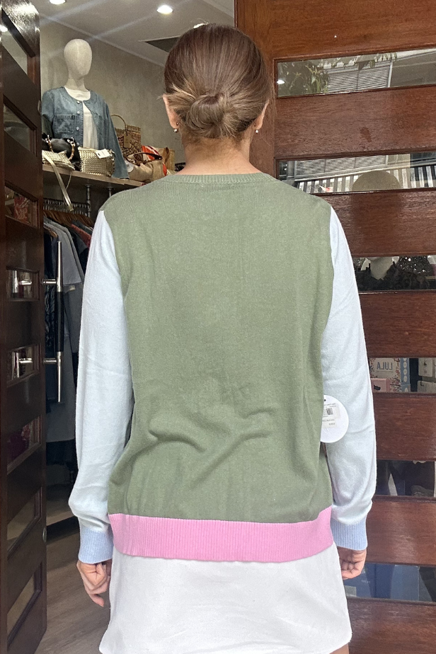 Person wearing a green vest over a white shirt with pink trim, standing in front of a wooden door.