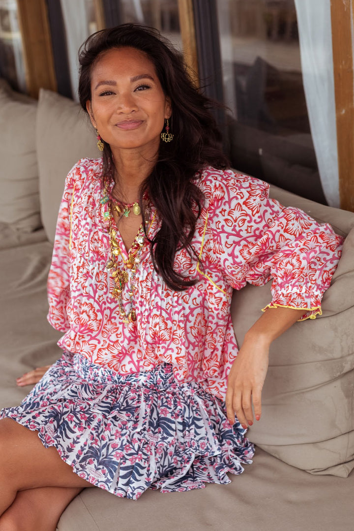 A woman wearing a pink and white patterned bohemian-style top and matching patterned skirt sits on a beige outdoor sofa.