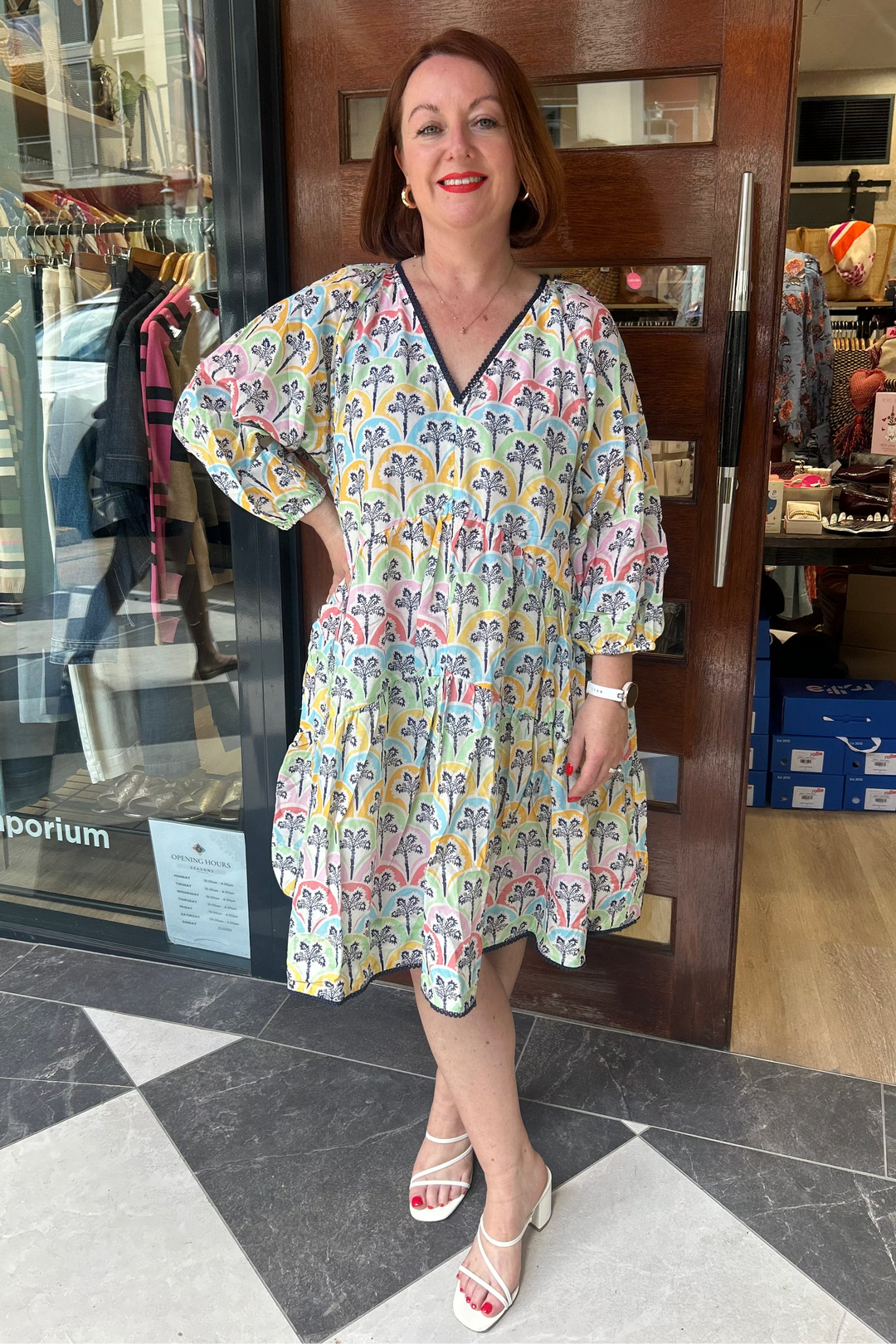 Woman in a colorful dress standing in front of a store entrance.