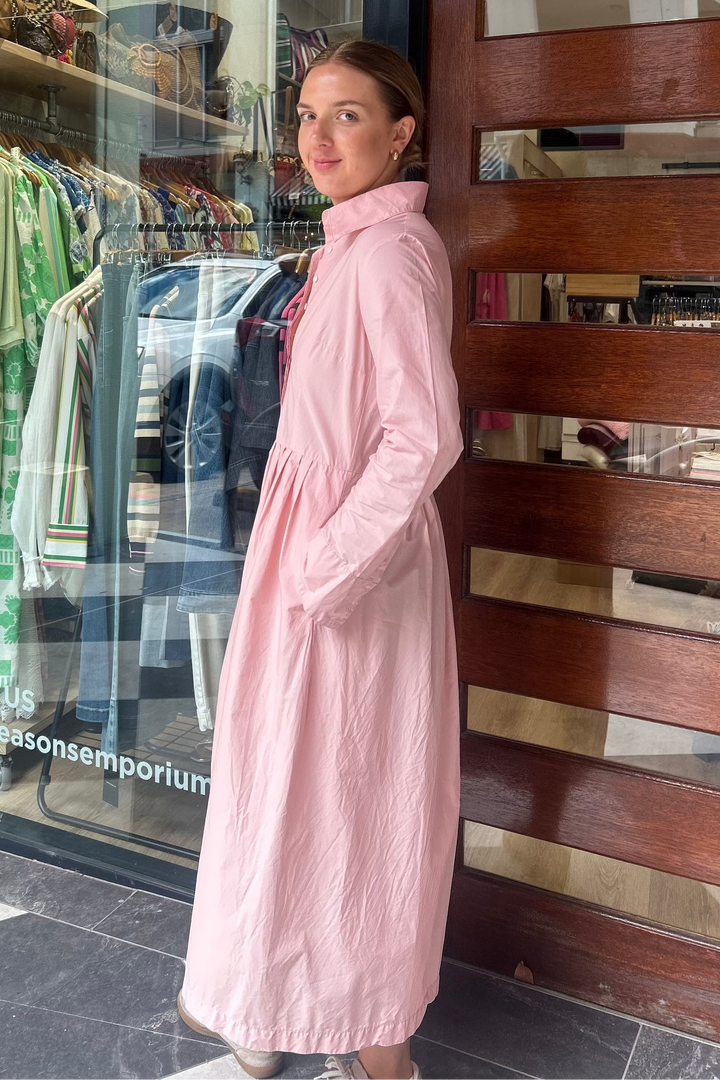 Woman in a pink coat standing outside a store with a glass door displaying clothing.