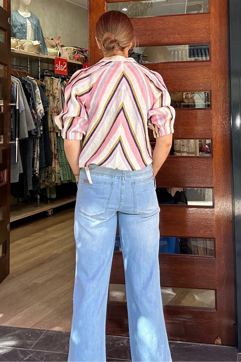 Person standing outside a clothing store with a colorful logo on the door.