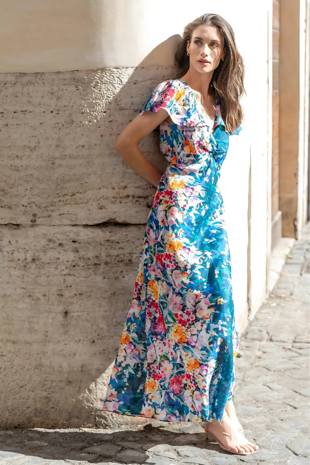 Woman in a colorful floral dress standing against a stone wall.