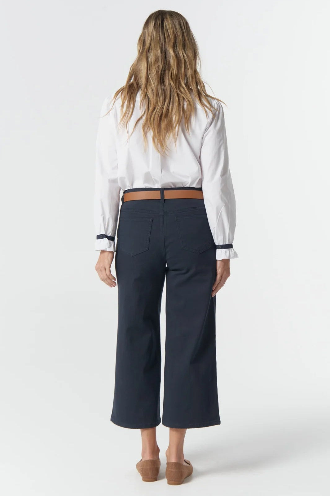 Woman wearing a white blouse and navy wide-leg pants on a white background