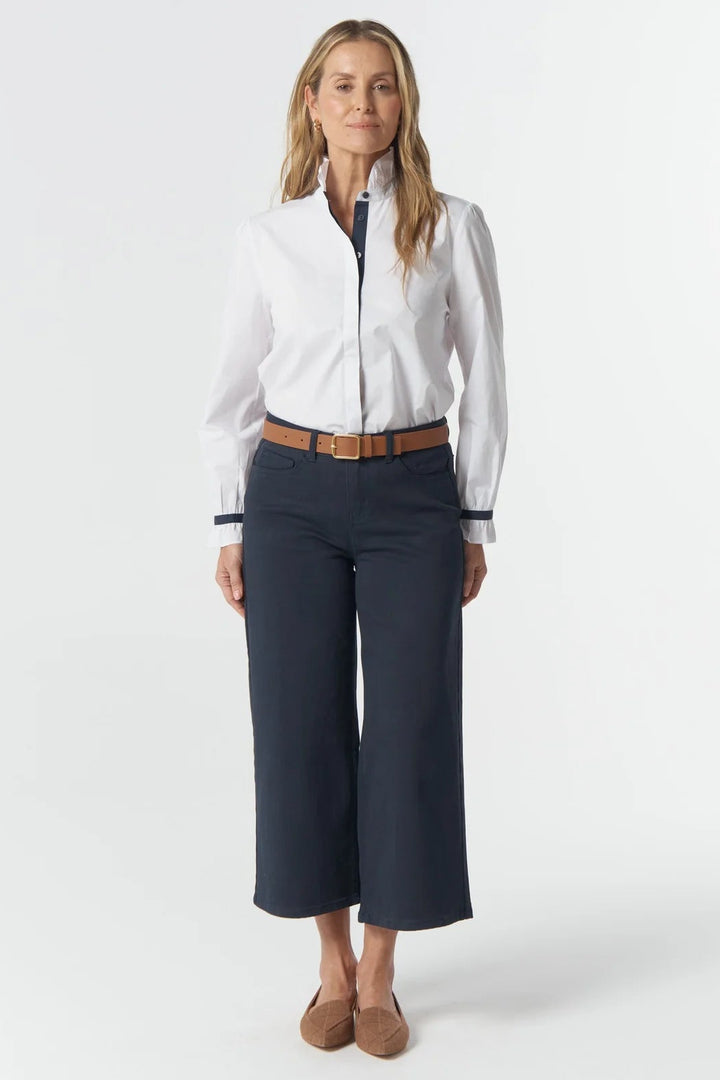 Woman wearing a white blouse with black trim and navy pants on a white background