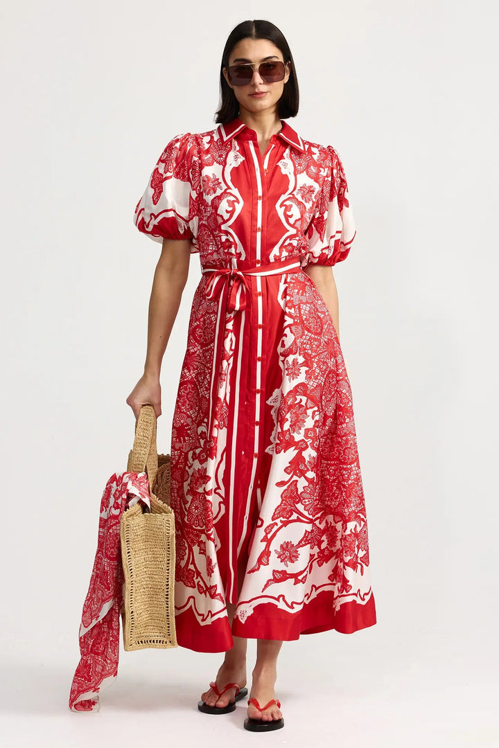 Woman wearing a red and white patterned dress holding a straw bag on a white background