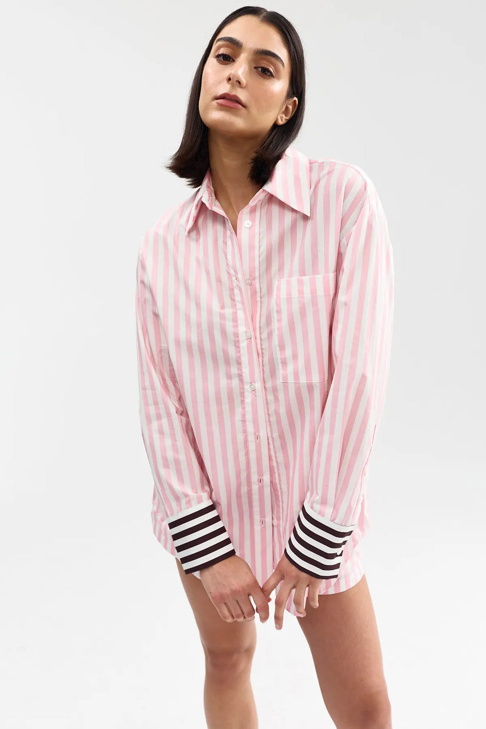 Woman wearing a pink and white striped shirt with black and white cuffs on a light gray background
