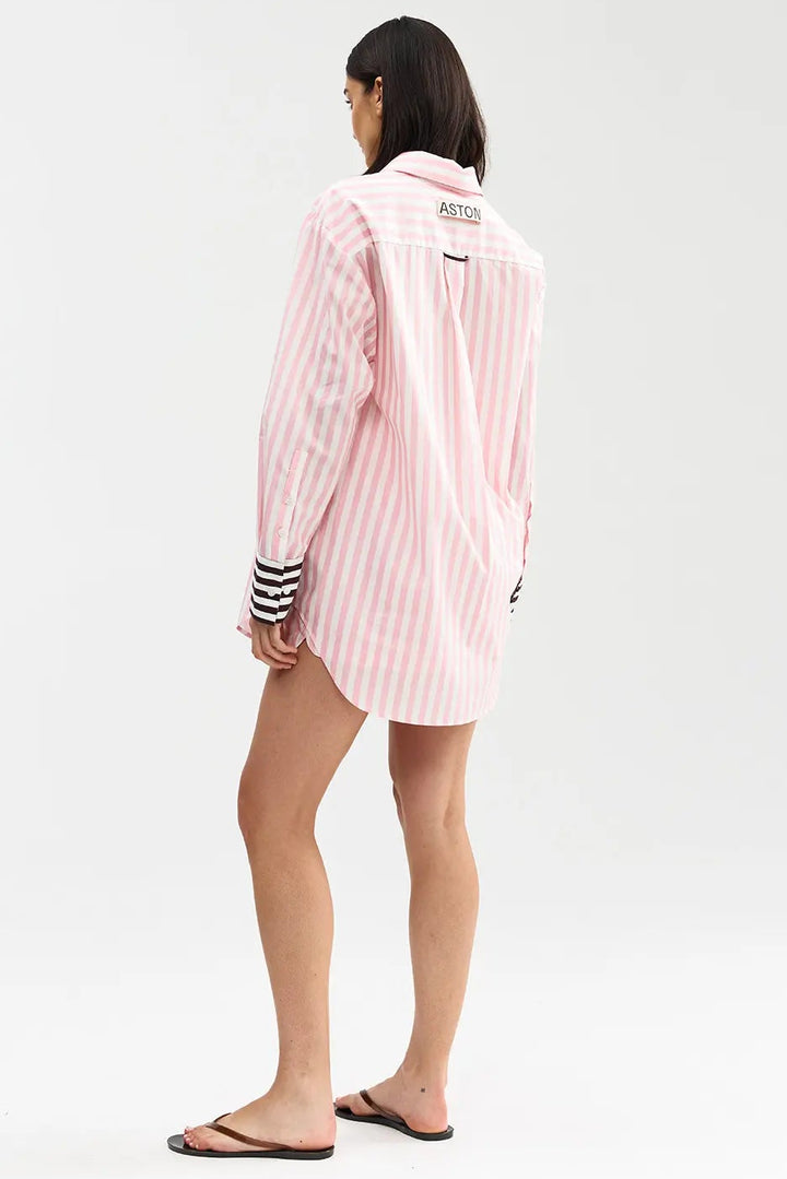 Person wearing a pink and white striped shirt with black trim on a white background