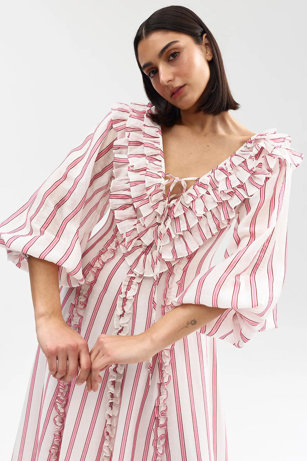 Woman wearing a pink and white striped dress with ruffled sleeves on a white background