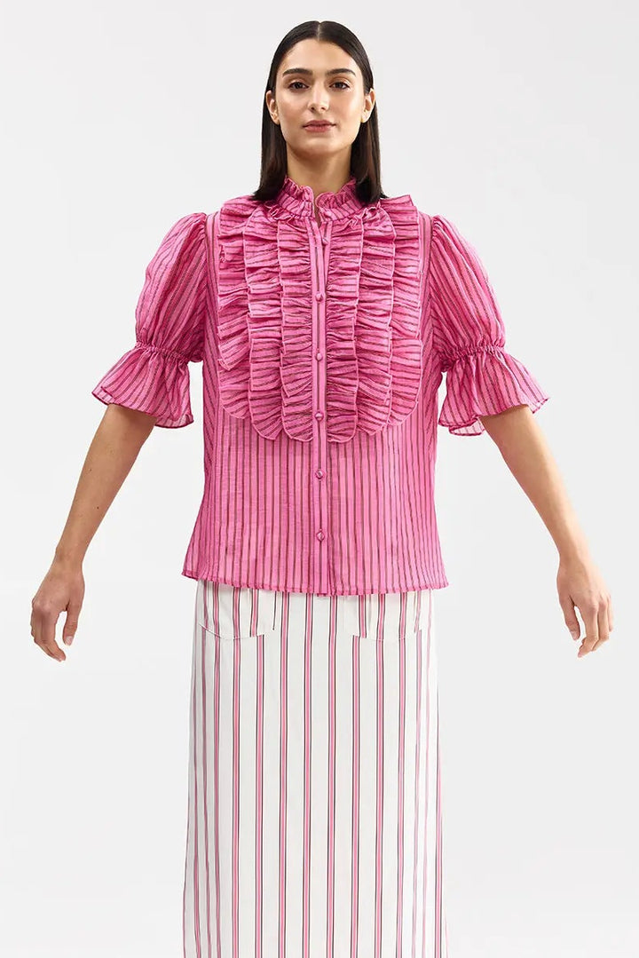 Woman wearing a pink ruffled blouse and white striped skirt on a white background