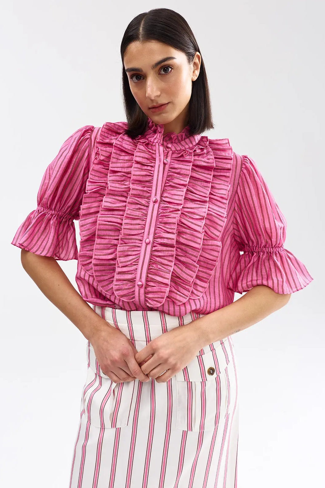 Woman wearing a pink ruffled blouse and striped pants on a white background