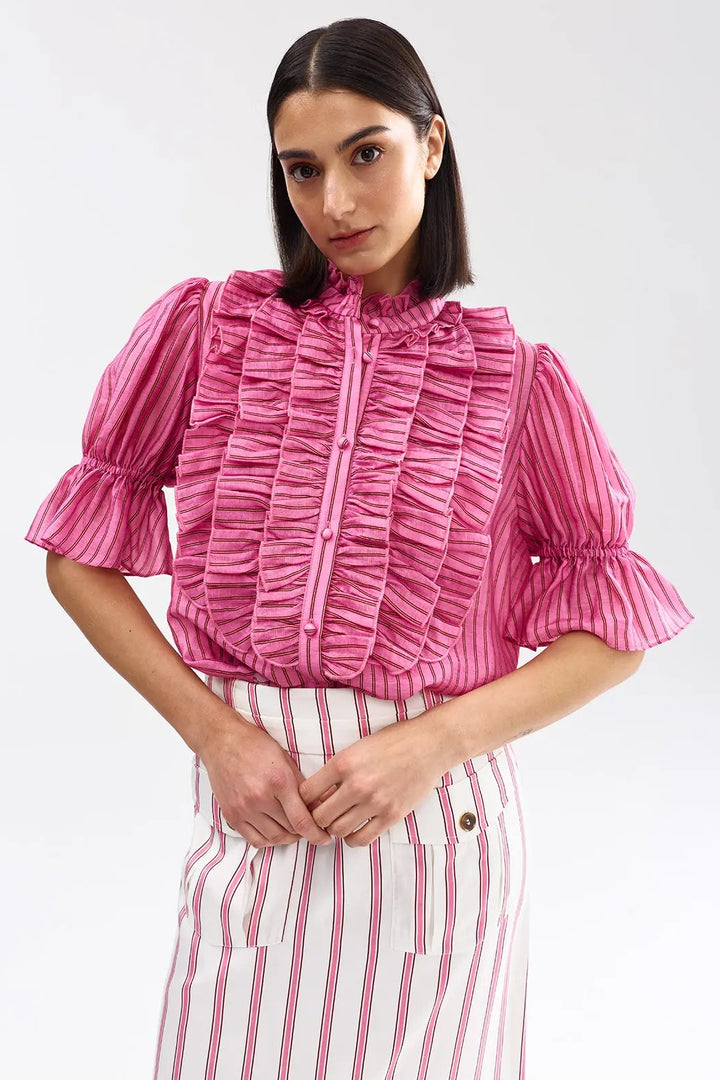 Woman wearing a pink ruffled blouse and striped pants on a white background