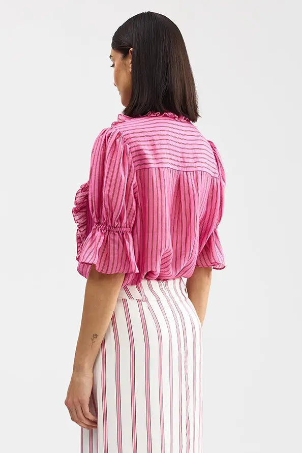 Woman wearing a pink striped shirt and white pants with red stripes on a white background