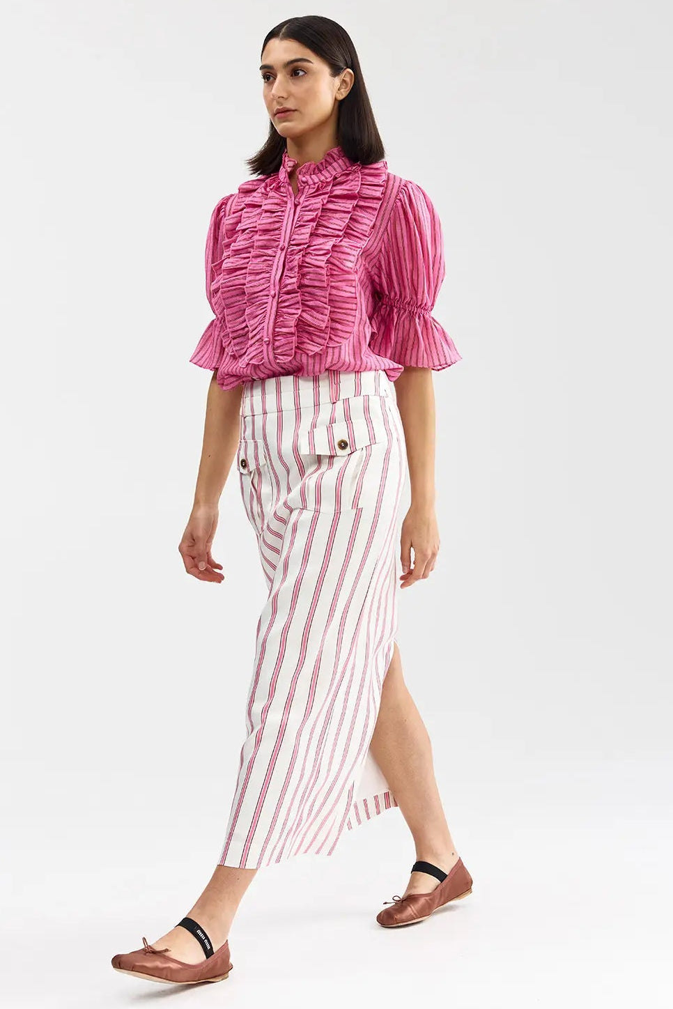 Woman wearing a pink ruffled blouse and striped pants on a white background
