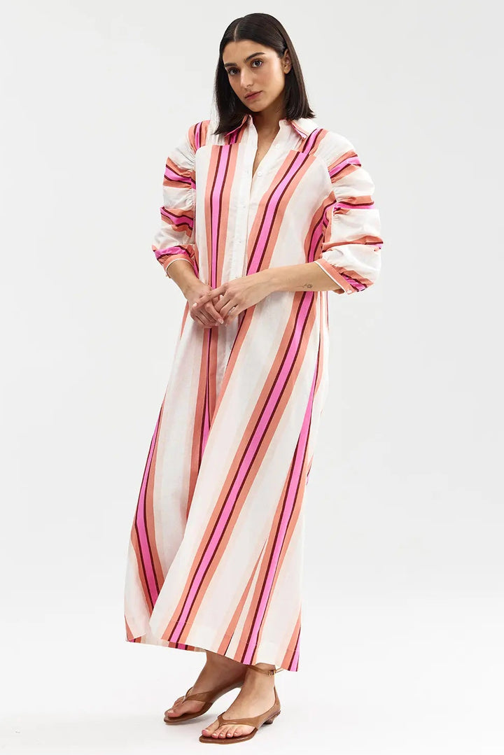 Woman wearing a long, striped dress with pink and orange stripes on a white background