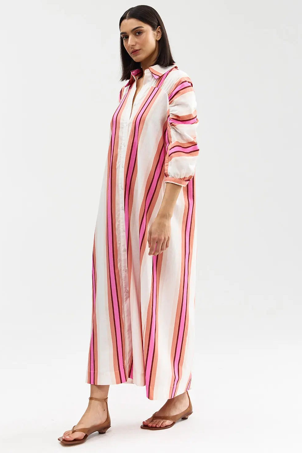 Woman wearing a long, striped dress with pink and white stripes on a white background