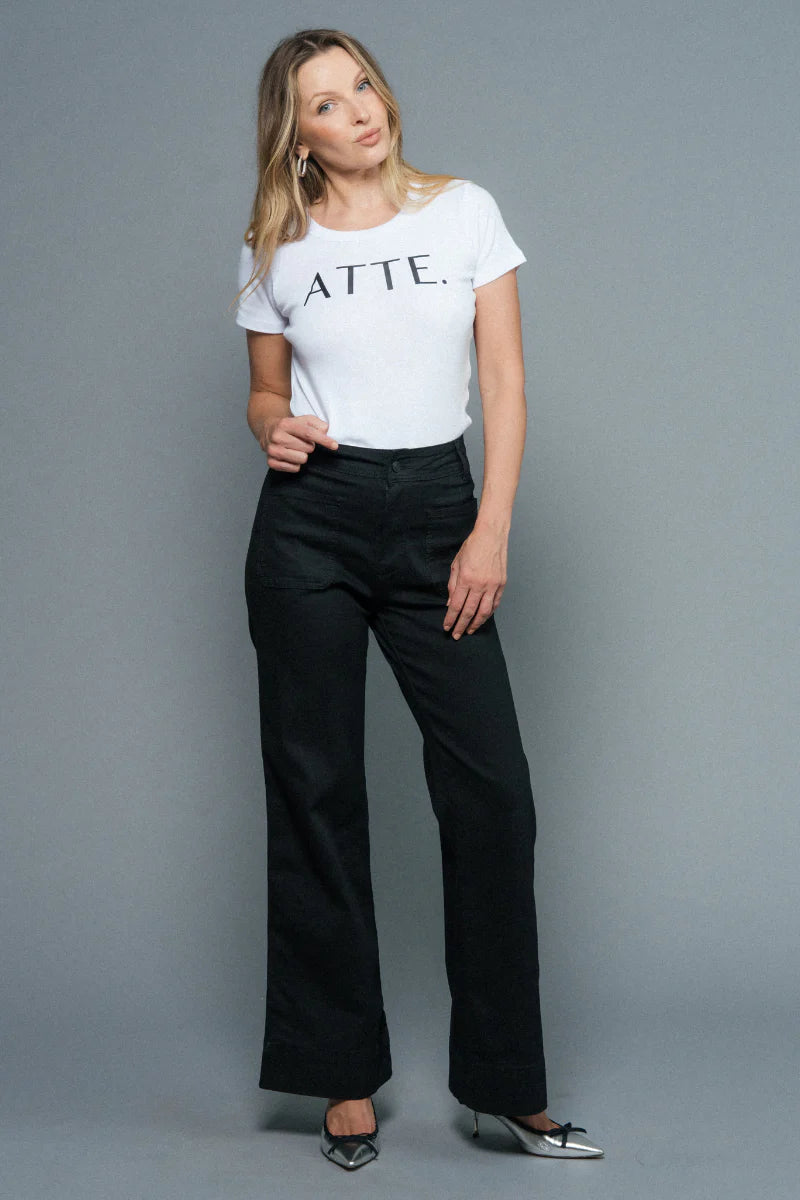 Woman wearing a white t-shirt with text and black pants on a gray background
