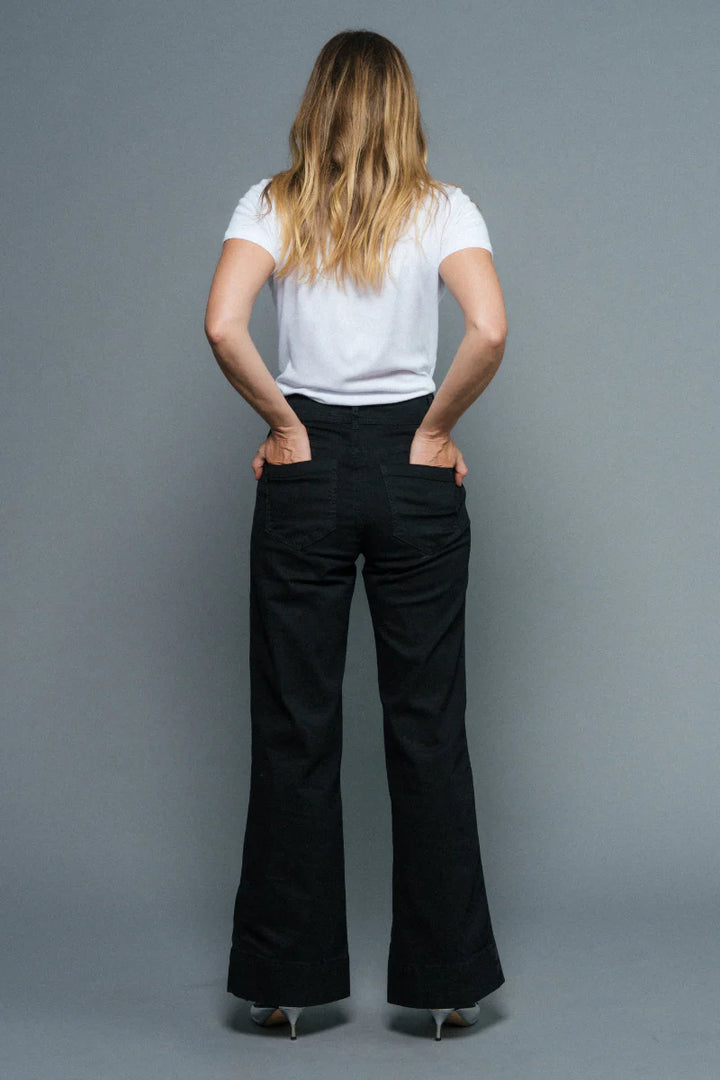 Person wearing a white top and black flared pants against a gray background