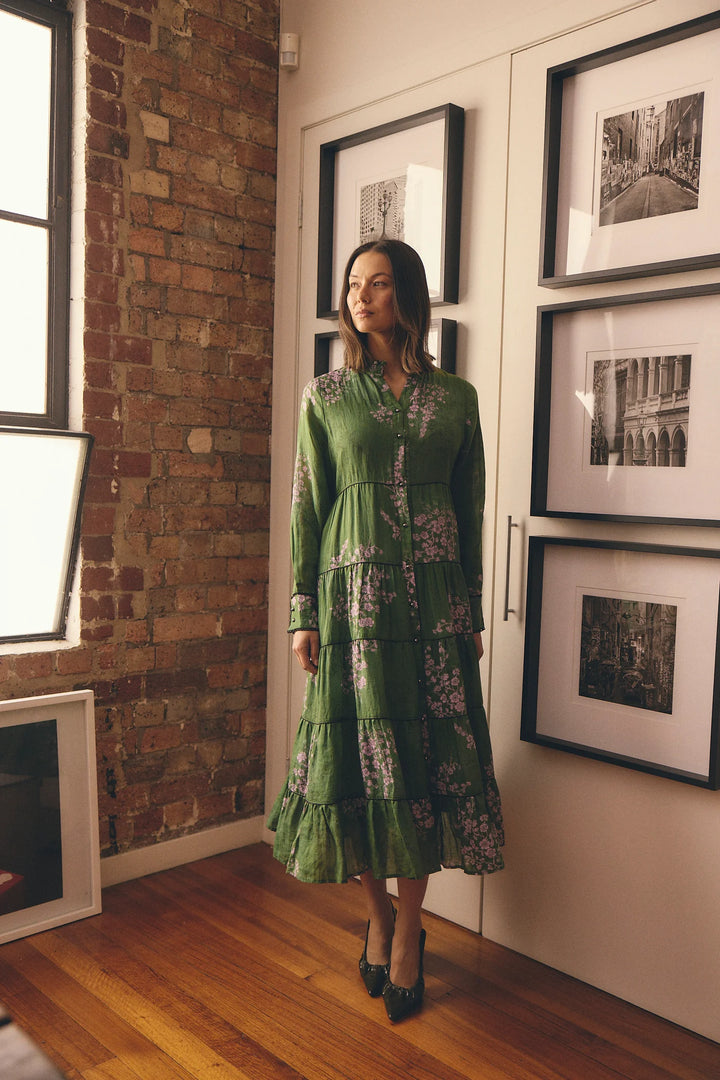 Woman in a green dress standing in a room with framed pictures on the wall.