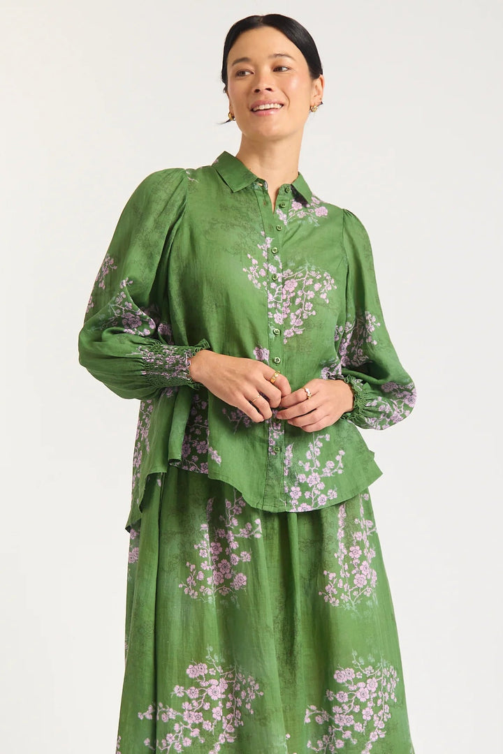 Woman wearing a green floral blouse and skirt on a white background