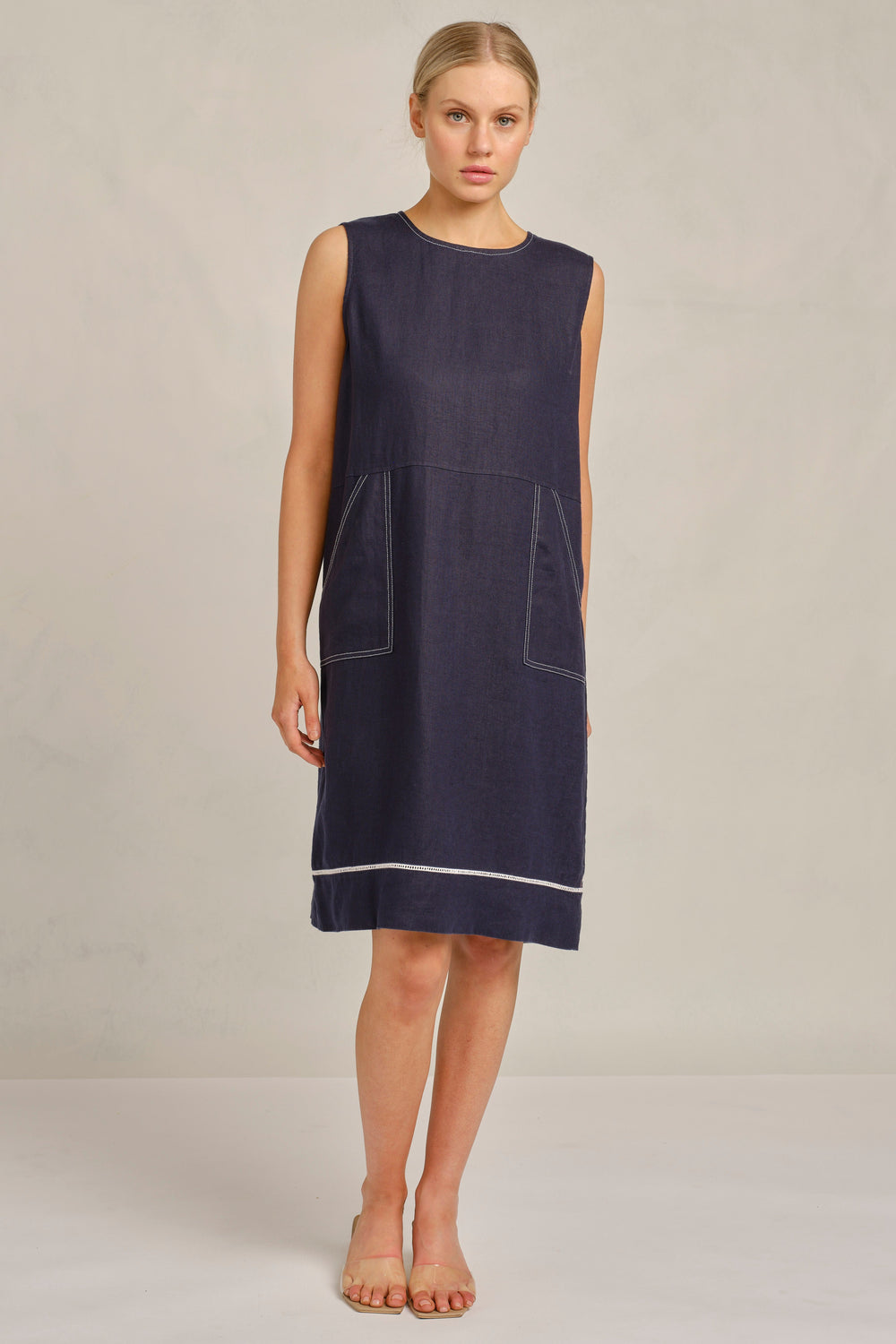 Woman wearing a navy sleeveless dress on a plain background