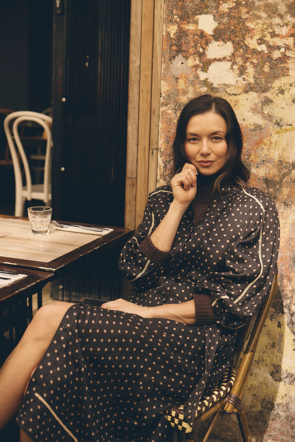 Woman sitting at a table in a rustic setting with a textured wall.
