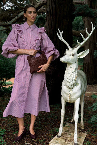 Woman in a purple dress standing next to a white deer statue in a forest setting