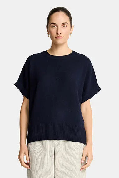 Woman wearing a navy blue top and beige pants on a white background