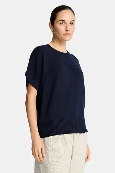 Woman wearing a navy sweater and beige pants on a white background