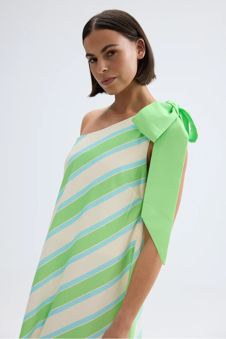 Woman wearing a green and white striped dress with a bow detail on a white background . Aston Studio Mila Dress Fern Lapis Stripe