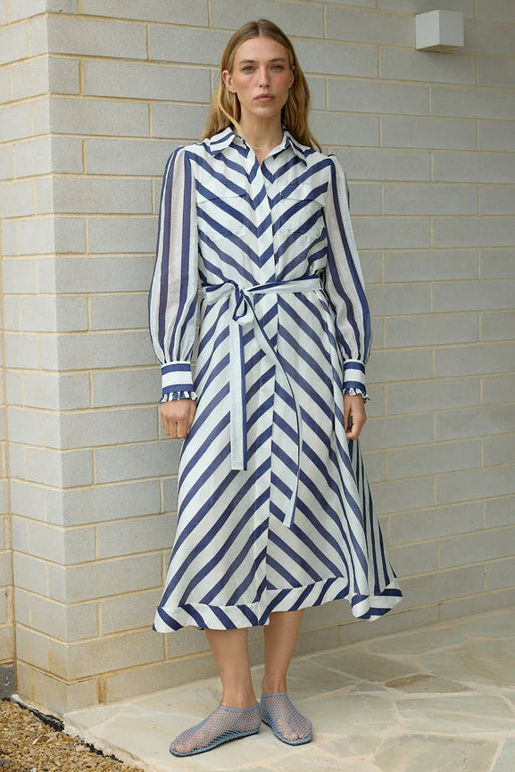 Woman wearing a blue and white striped dress standing against a brick wall.