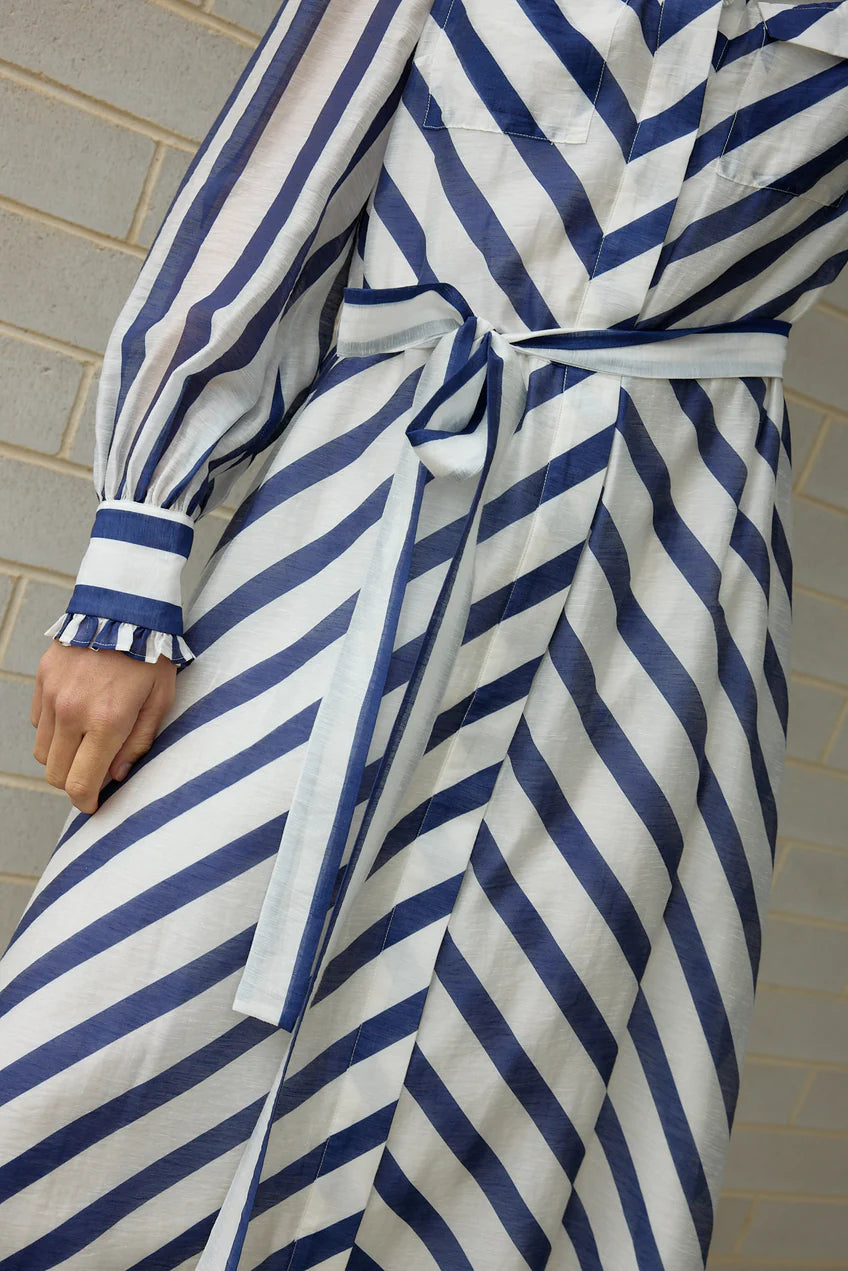Person wearing a blue and white striped robe against a tiled wall.