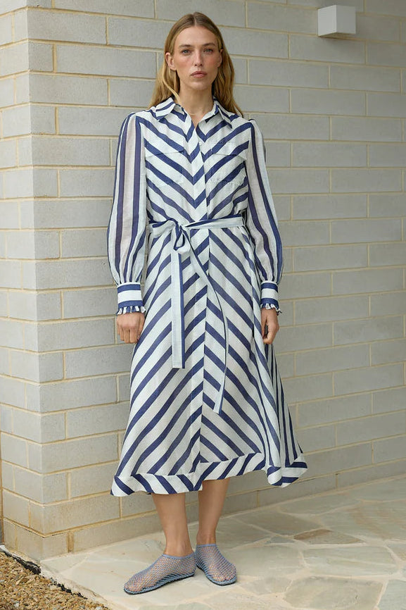 Woman wearing a blue and white striped dress standing against a brick wall.