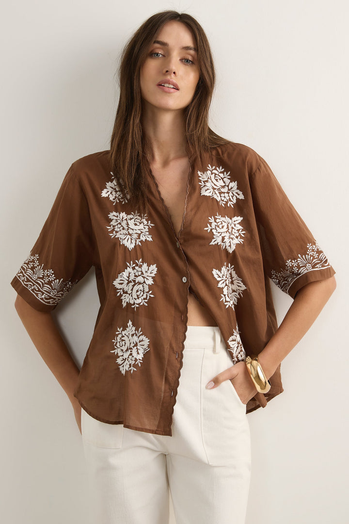 Woman wearing a brown blouse with white floral patterns against a plain background