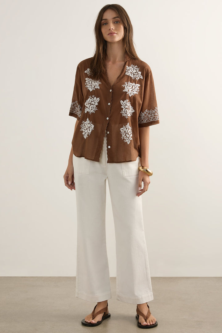 Woman wearing a brown floral shirt and white pants against a plain background