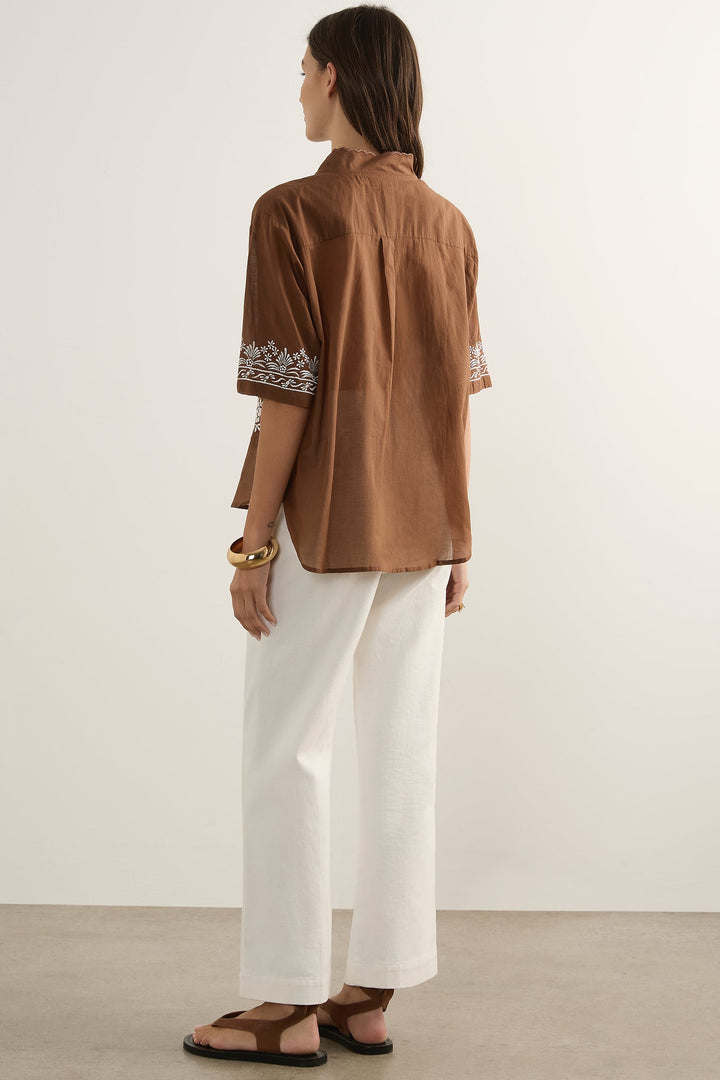 Woman wearing a brown blouse with white pants against a plain background