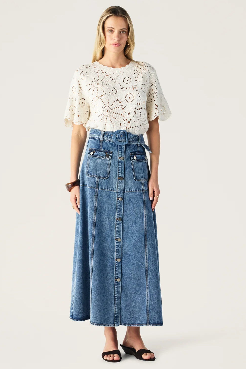 Woman wearing a white lace top and blue denim skirt on a white background