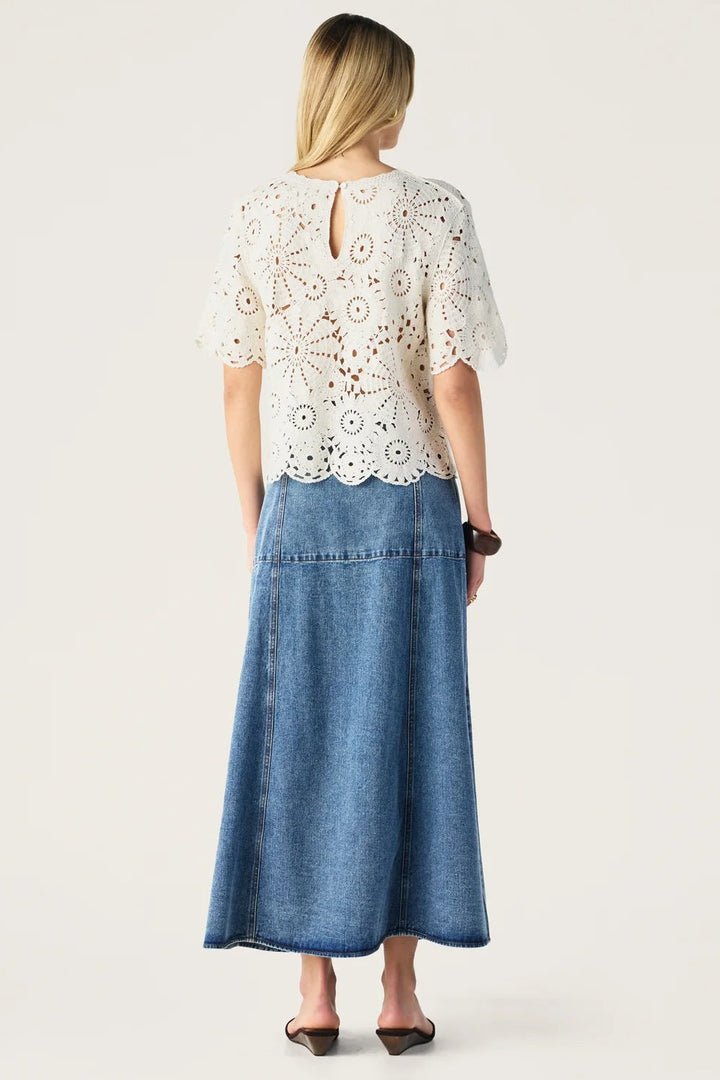 Woman wearing a white lace top and blue denim skirt on a white background