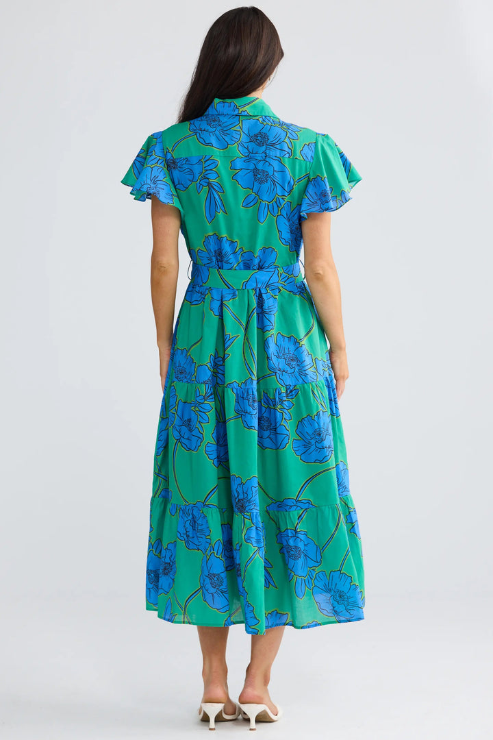A woman viewed from behind wearing a green midi dress with a blue floral print, short flutter sleeves, and a matching waist tie, set against a plain light gray studio background.