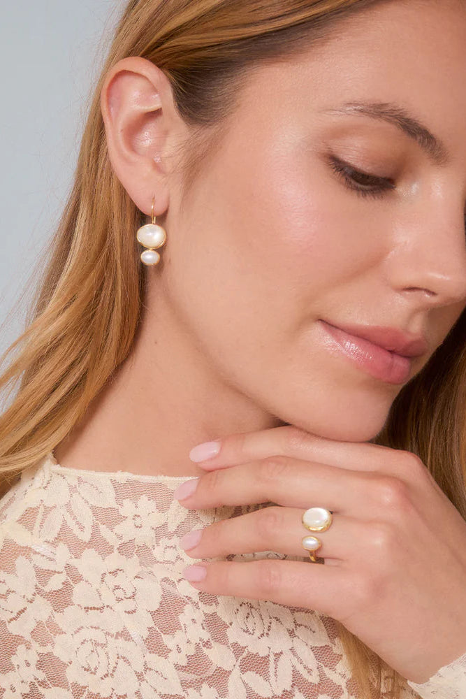 Woman wearing pearl earrings and ring against a neutral background