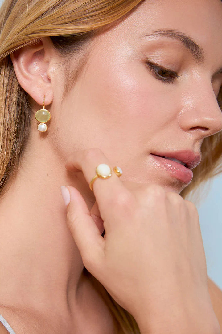 Woman wearing gold earrings and a ring with a light blue background