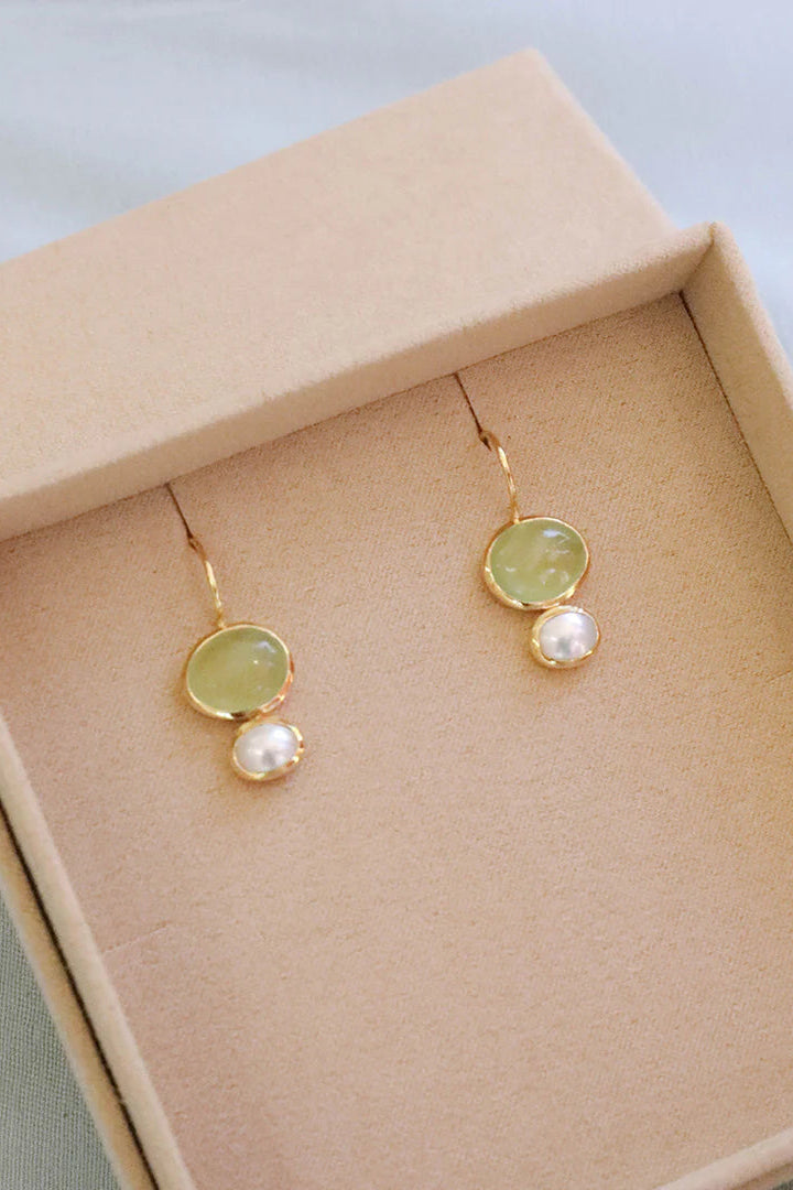 Pair of earrings with green stones and pearls in a beige jewelry box.