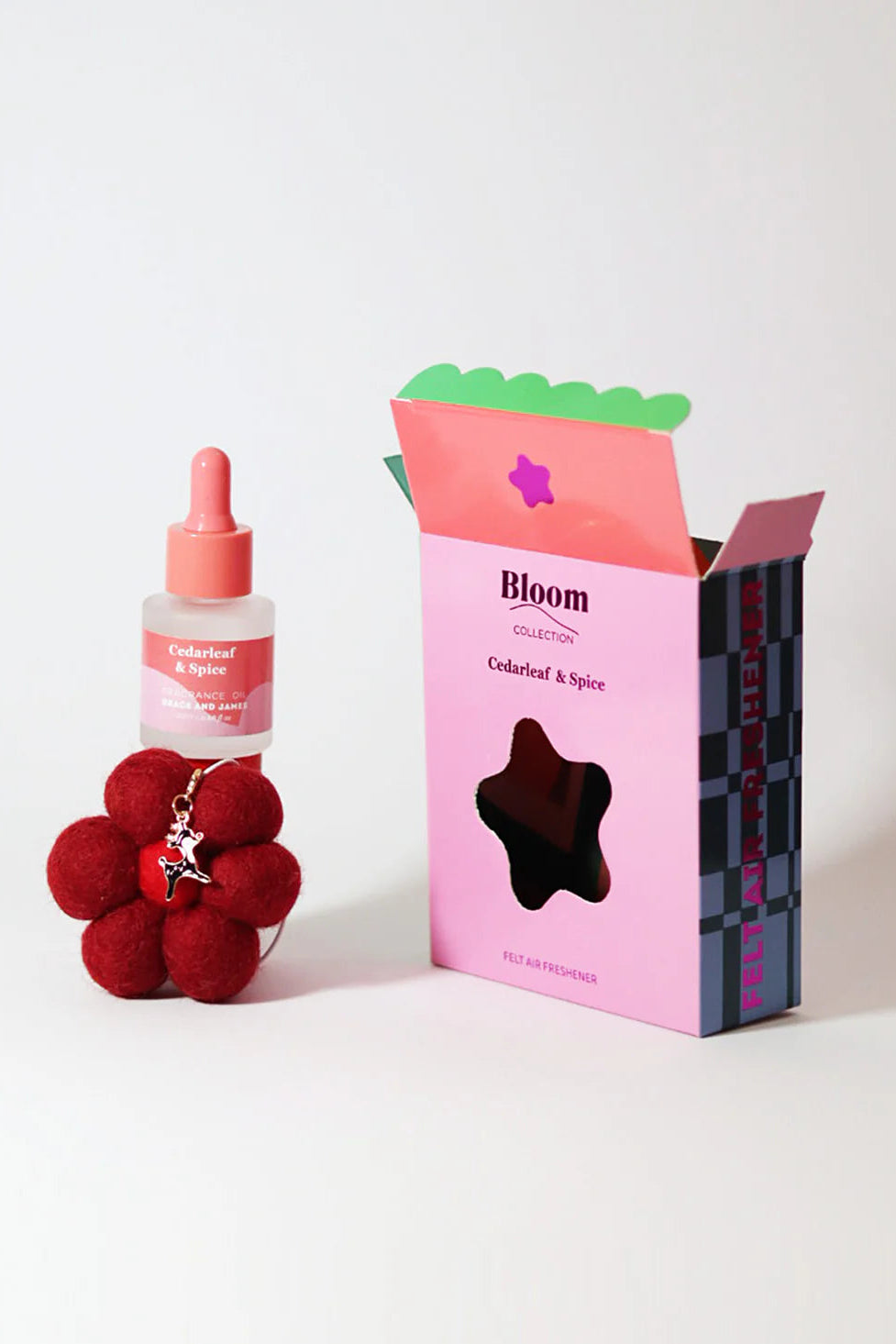 Fragranced oil with dropper, red flower-shaped felt air freshener, and pink box labeled 'Bloom' on a white background. Cedarleaf & Spice