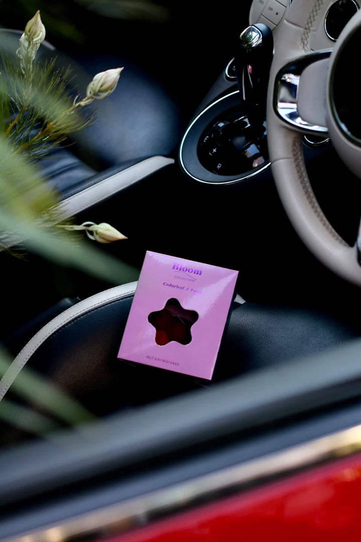 Pink car air freshener with star-shaped scent disc on a car dashboard. Cedarleaf & Spice