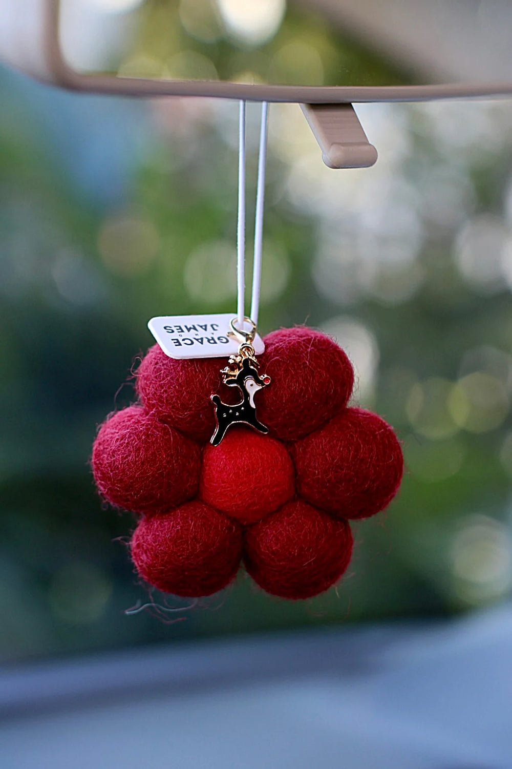 Red flower shapped felt airfreshener with a reindeer charm hanging from a car mirror. Cedarleaf & Spice