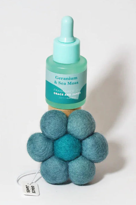 Teal bottle with fragranced oil dropper and matching teal flower shaped felt airfreshener on a white background