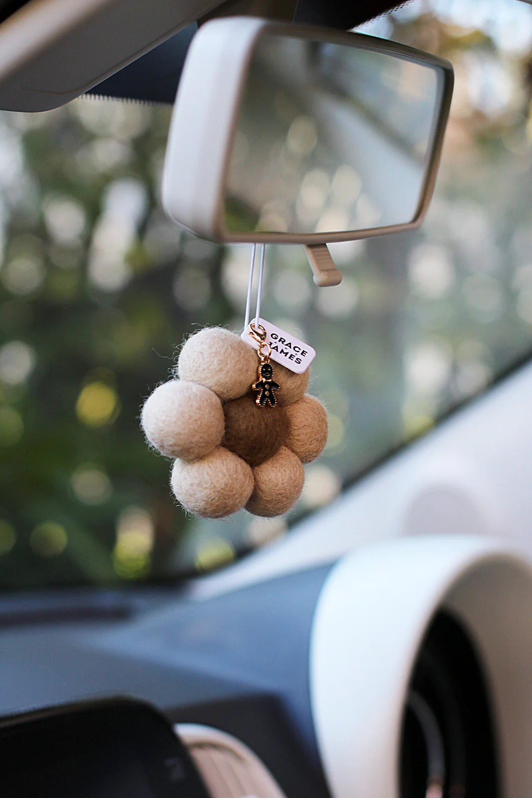 Car rearview mirror with a flower shaped felt air freshener hanging from it.