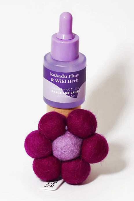 Purple fragranced oil bottle with dropper and purple and pink flower shaped felt air freshener on a white background