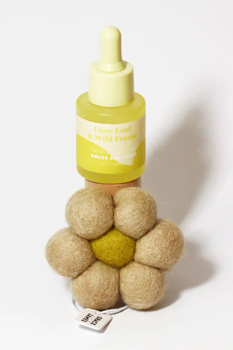 Yellow bottle with a fragranced oil dropper and flower shaped felt air freshener on a white background. Lime leaf & fresia