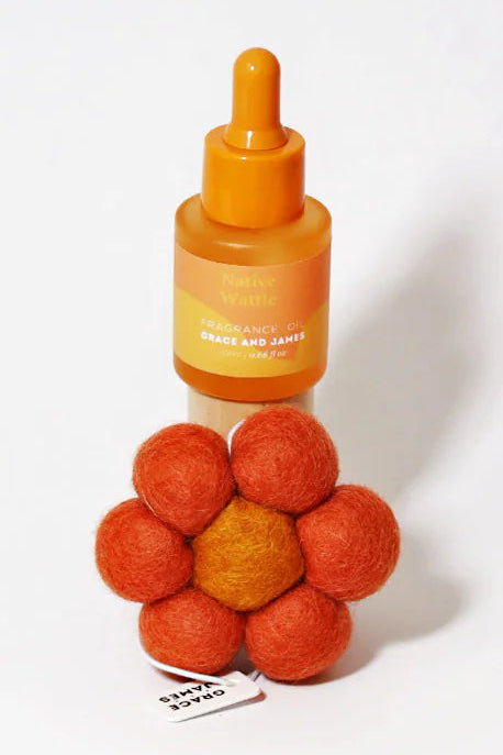 Orange fragranced oil bottle with dropper and flower shaped felt air freshener on a white background