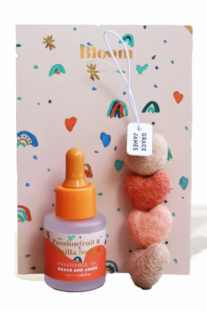 Bottle of fragranced oil with a heart shaped felt string air freshener on a colorful card with 'Bloom' branding.